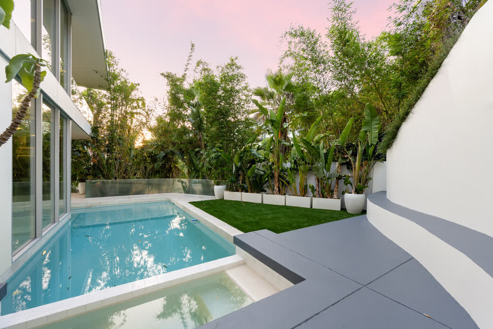Modern pool space with grey tiles and concrete walls and planter boxes and native planting 